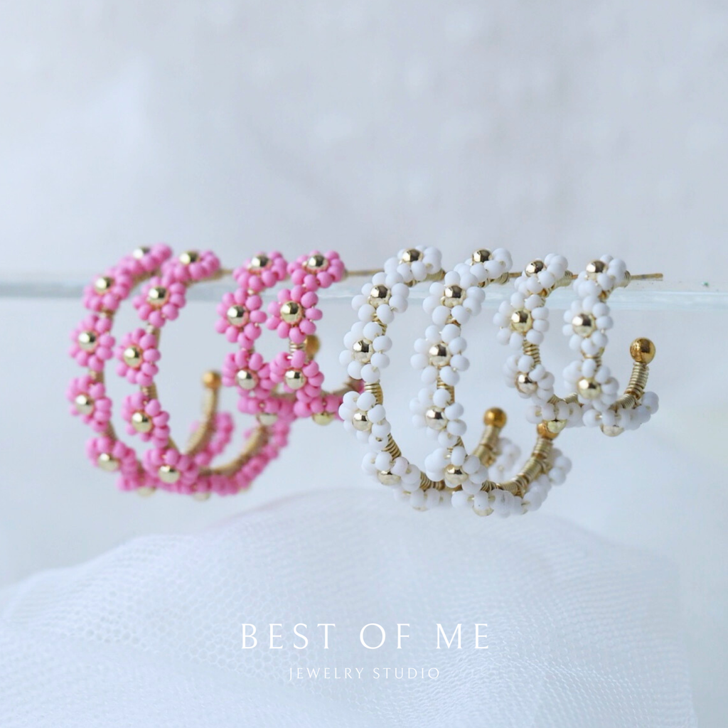Two beaded headbands, one pink and one white with gold accents, on a white surface.