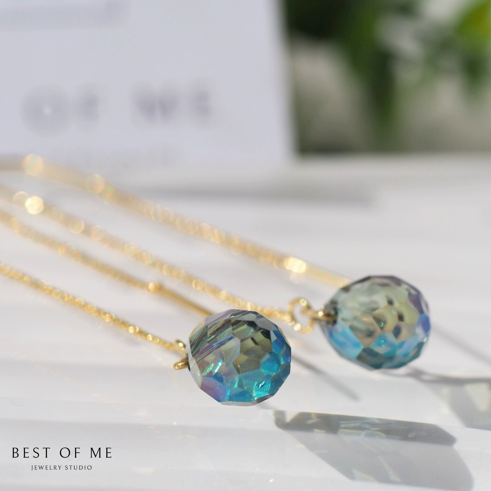 Gold earrings with green grey gemstones on a white surface, branded 'Best of Me Jewelry Studio'