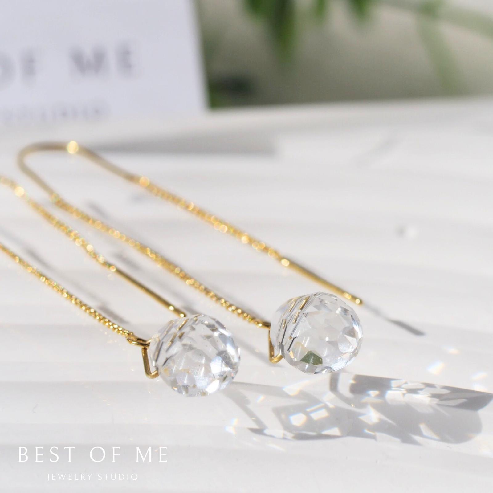 Gold ear thread with clear  glass beads on a white surface, branded 'Best of Me'.