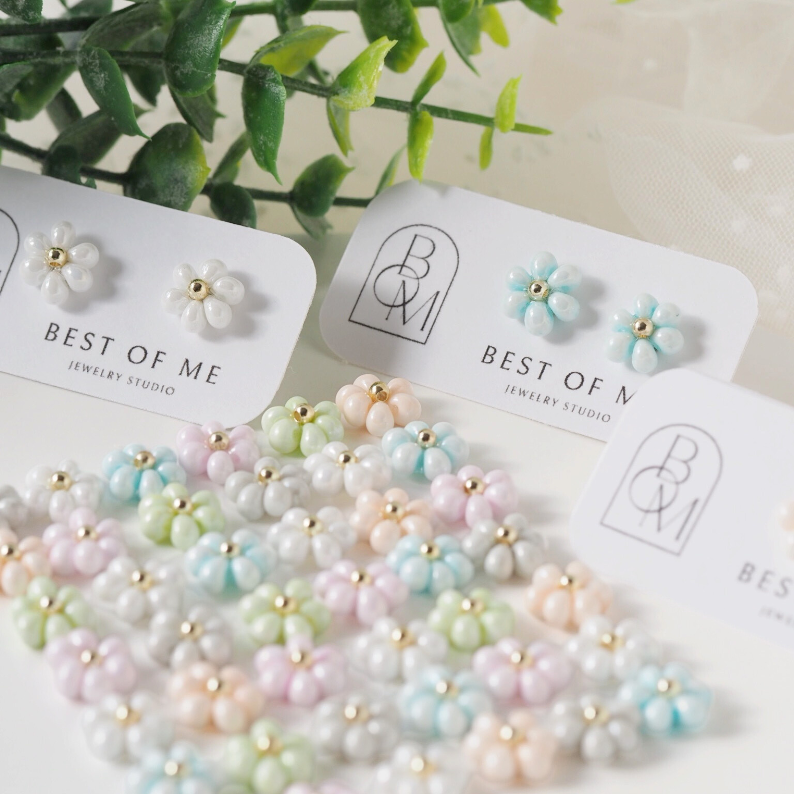 Pastel-colored delicate floral earrings on display with 'Best of Me Jewelry Studios' packaging.