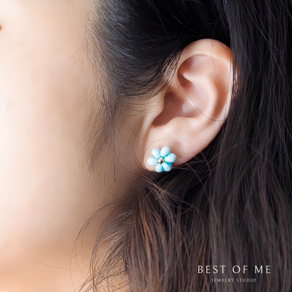 Close-up of an ear wearing a blue flower-shaped earring with blurred background