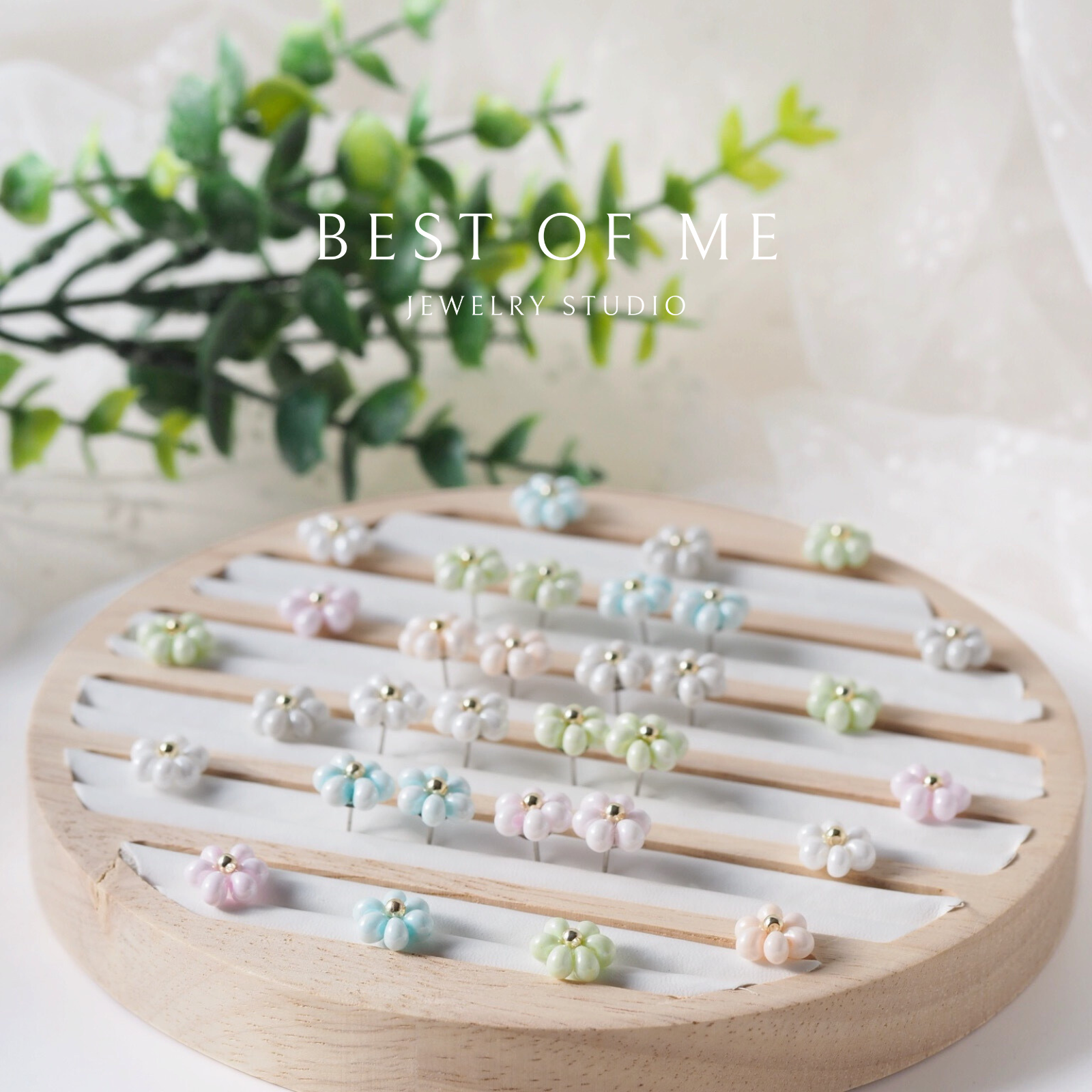 Wooden display board with pearl earrings on a white surface with greenery in the background, featuring 'Best of Me Jewelry Studio'.