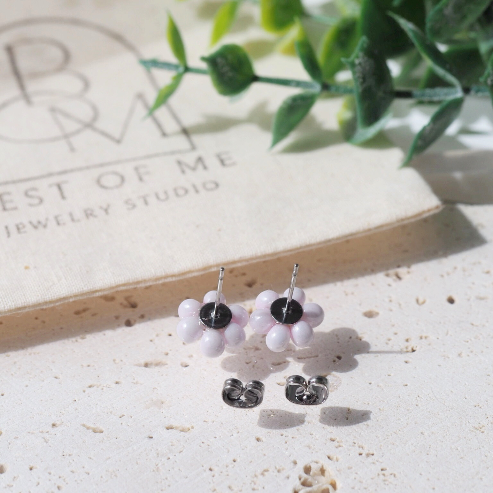 Flower-shaped earrings on a textured surface with a brand name jewelry bag in the background.