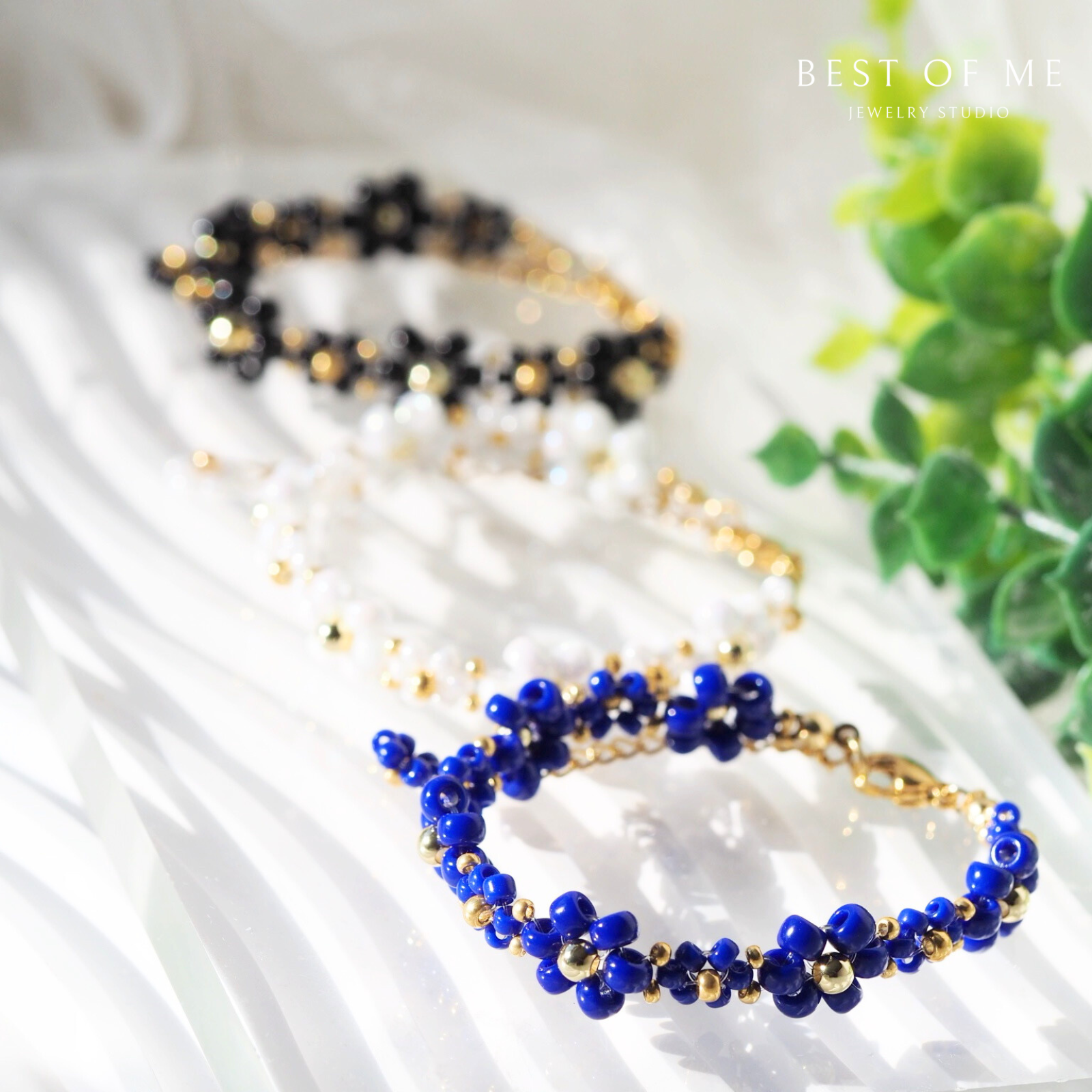three elegant flower bracelets on a white surface with a plant in the background