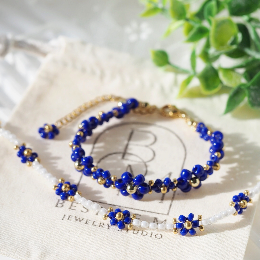 Blue and gold beaded bracelets on a white surface with a blurred plant in the background
