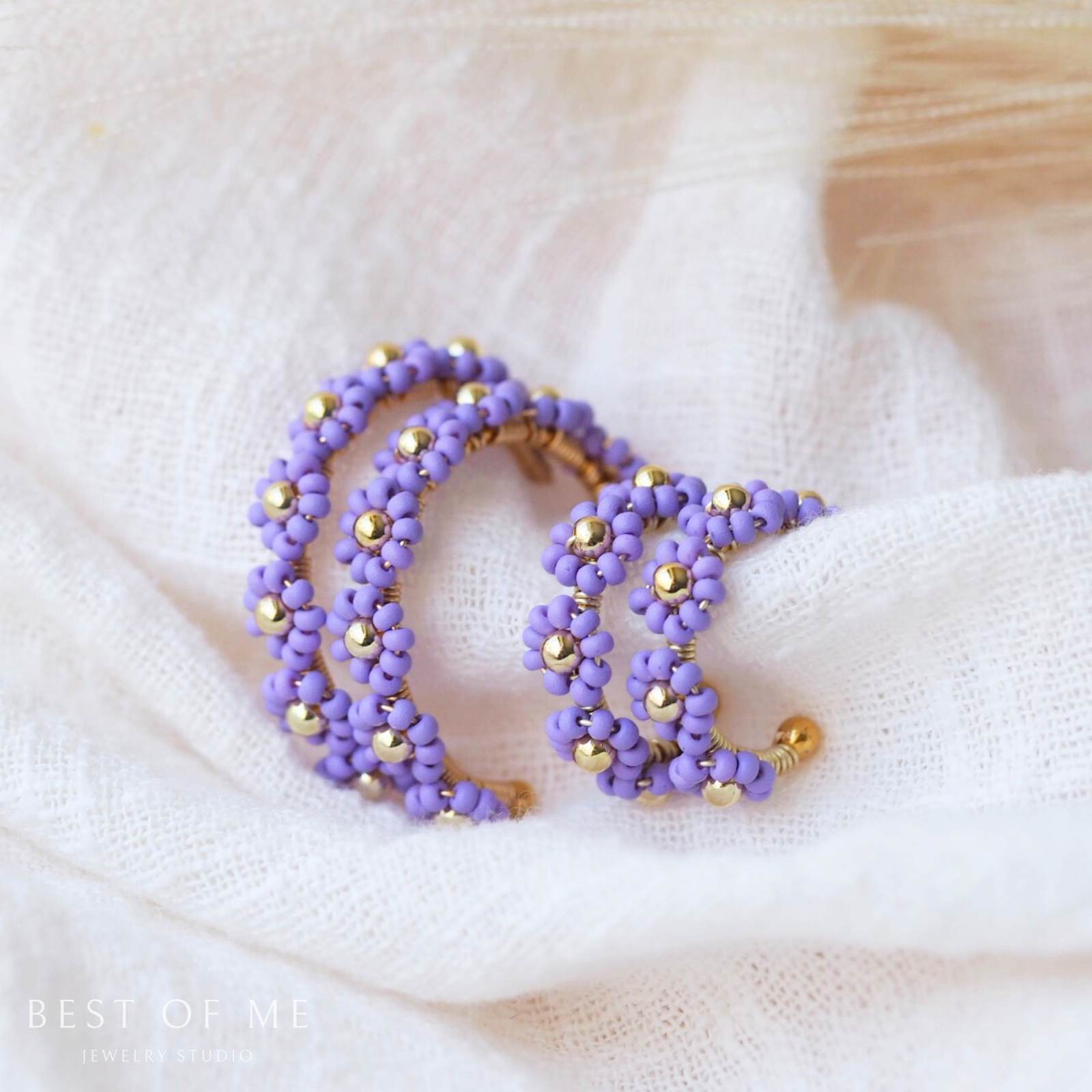 Purple beaded flower earrings  with gold accents on a soft white fabric background