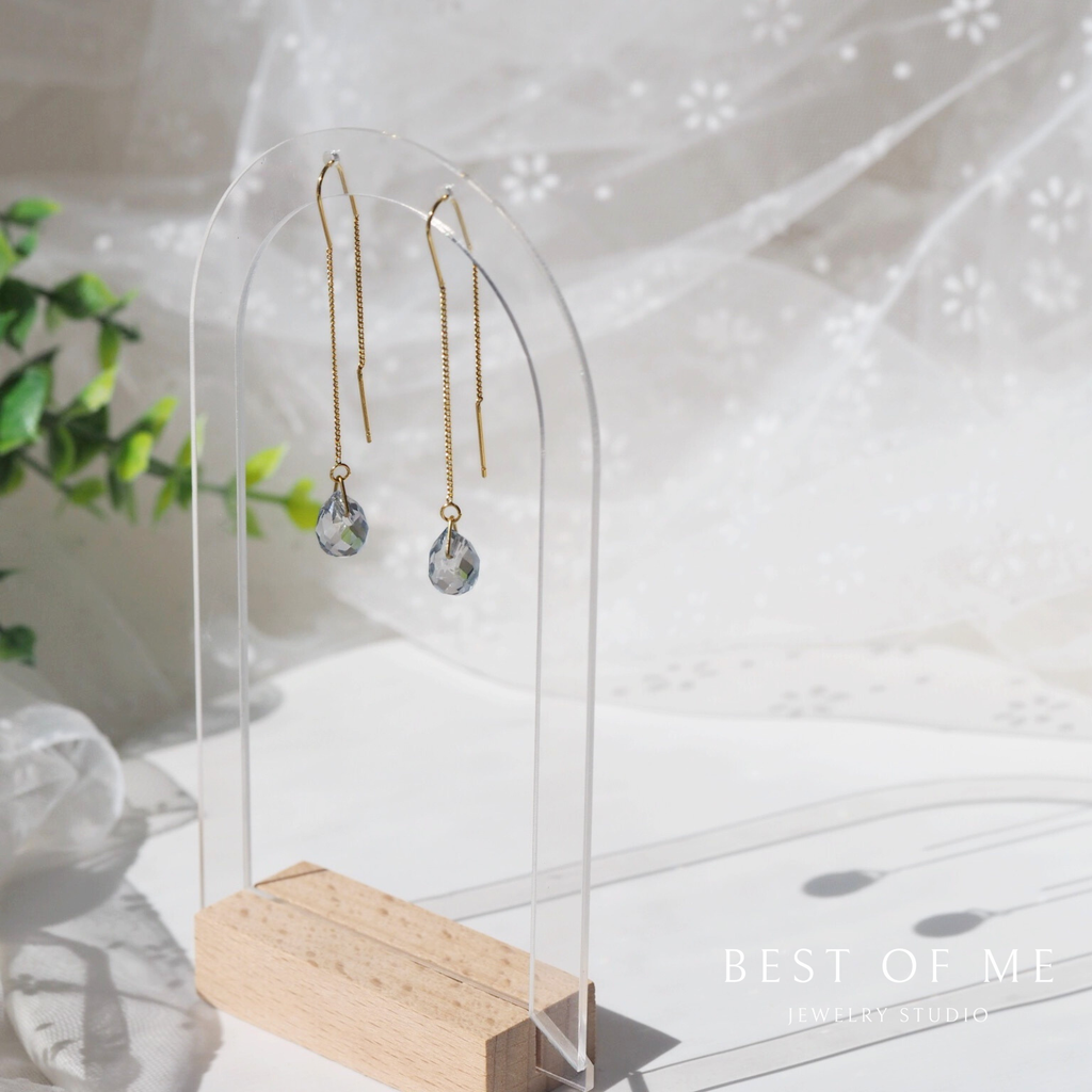 Gold earrings with clear beads on a wooden stand against a soft white background.