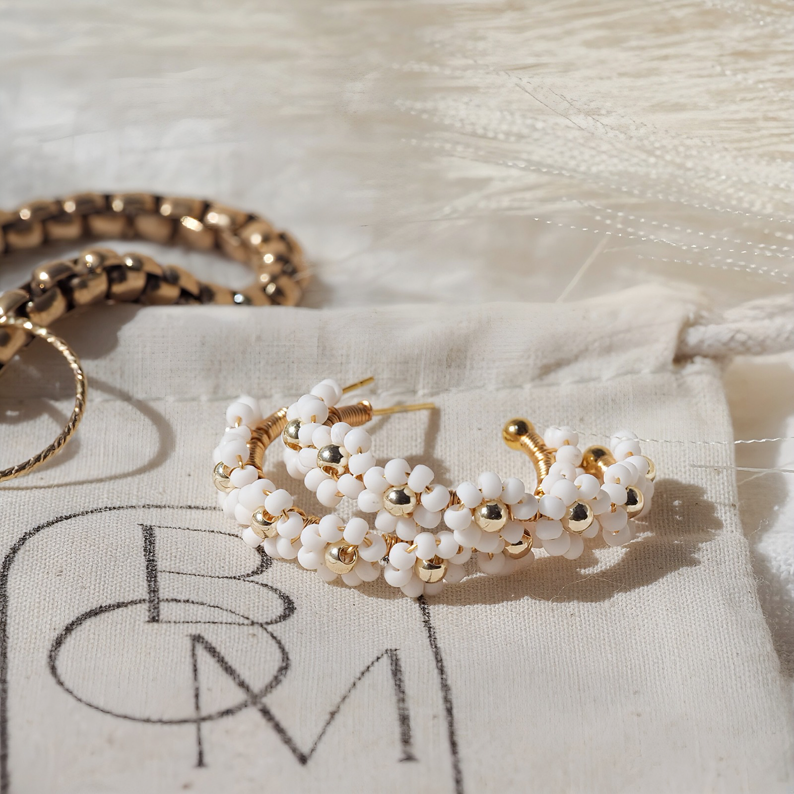 Gold and white beaded flower earrings on a brand logo jewelry bag 