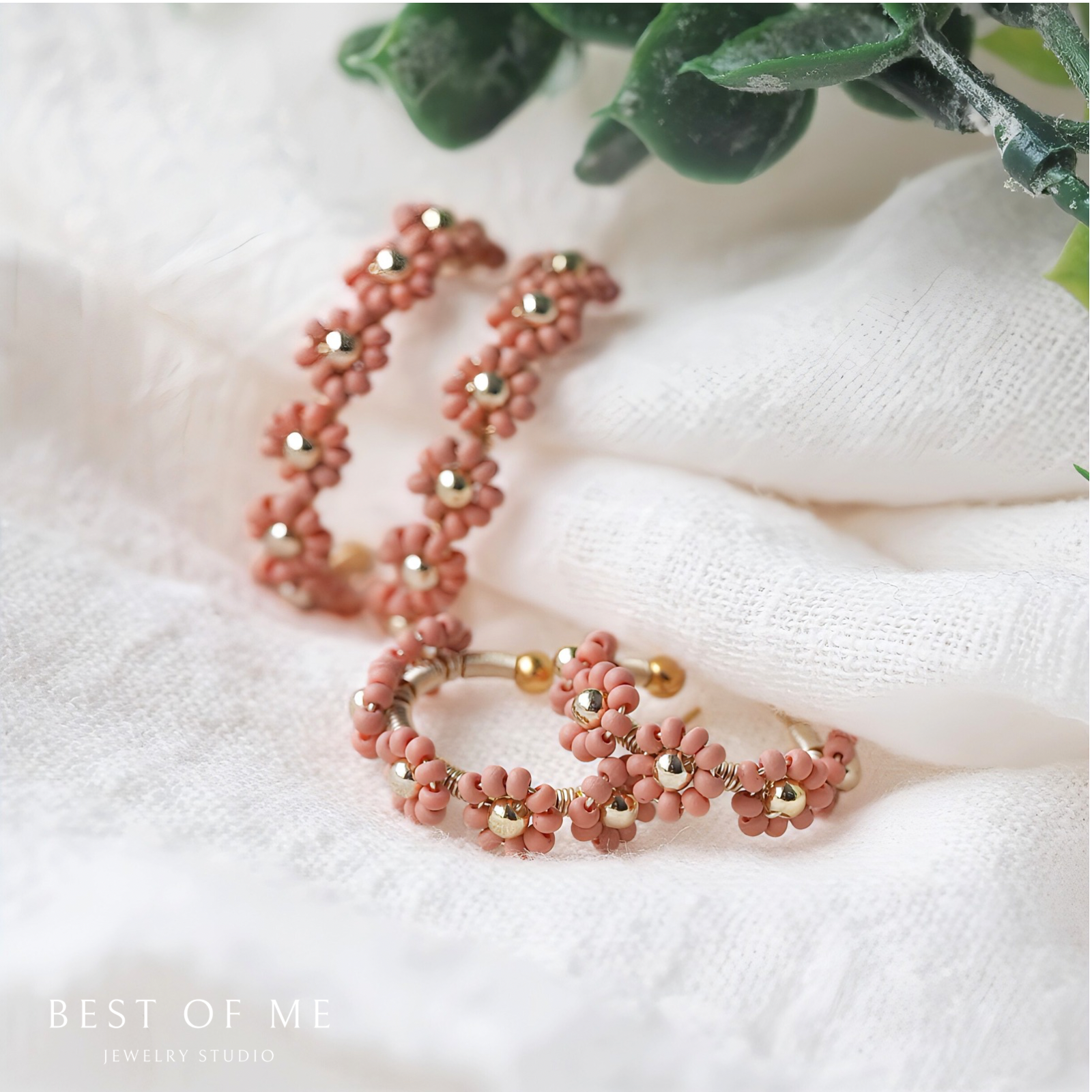 Pink beaded flower earrings with gold accents on a white fabric background