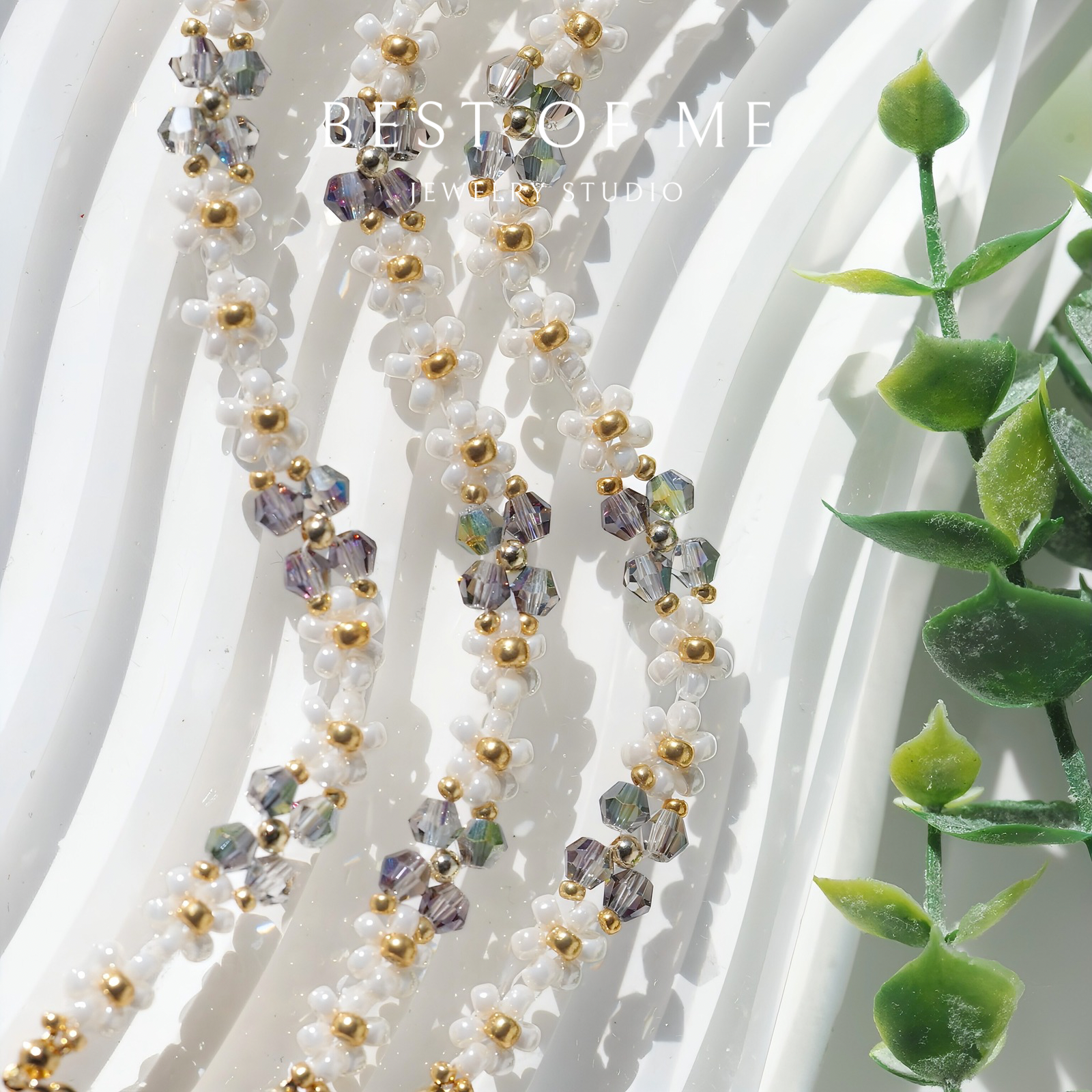 handmade bracelet with beads and crystals on a white background with green leaves.