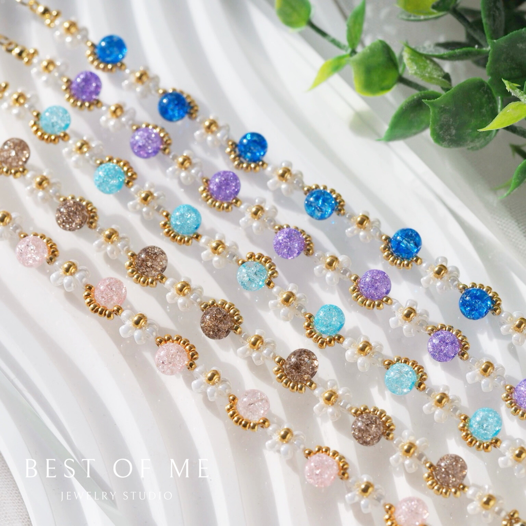 Colorful beaded jewelry on a white surface with green leaves in the background